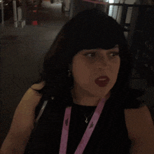 a woman wearing a lanyard that says ' shagarita ' on it stands in front of a sign that says wait