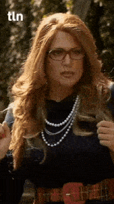 a woman wearing glasses and a pearl necklace is standing in front of a sign that says tln