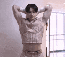 a man is standing in a room with his hands behind his head wearing a crop top and gloves .