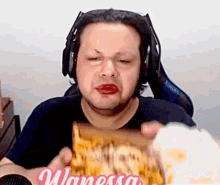 a man wearing headphones and red lipstick is eating a sandwich with the name vanessa on it