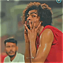 a man with curly hair is covering his face with his hands while another man looks on .