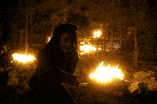 a woman holding a torch in front of a fire