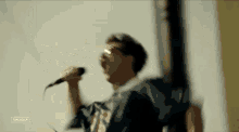 a man is singing into a microphone while wearing sunglasses and a blue jacket .