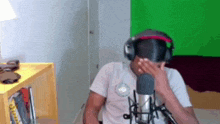 a man wearing headphones is covering his face while sitting in front of a microphone .