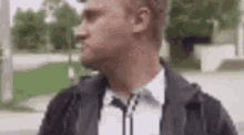 a man in a black jacket and white shirt is standing on a sidewalk .