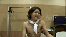 a shirtless man with a white towel around his neck smiles in front of a sign that says ' a ' on it