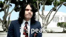 a man in a suit and tie says " it 's peak " in front of trees