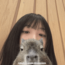 a girl holds a capybara in front of her face with the caption capybara yeojin disapproves