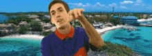 a man in a blue and red shirt is pointing to his ear in front of a beach