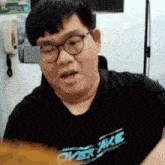 a man wearing glasses and a black shirt that says overake