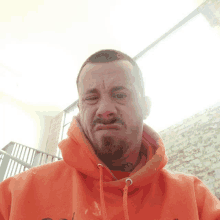 a man with a beard wearing an orange hoodie is making a funny face