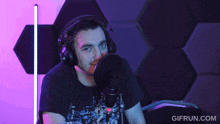 a man wearing headphones stands in front of a microphone with gifrun.com written in the corner