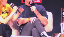 a man is sitting in a chair talking into a microphone while a woman looks on
