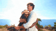 a man in a white shirt is hugging a woman in a straw hat