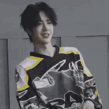 a young man wearing a black and yellow hockey jersey is smiling and holding a hockey stick .
