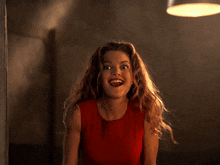 a woman in a red tank top holds her finger to her mouth