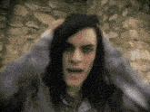 a man with long black hair is making a funny face in front of a stone wall