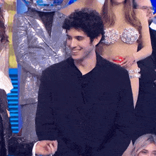 a man in a black suit is smiling in front of a disco ball