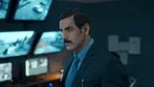 a man in a suit and tie stands in front of a monitor