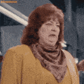 a woman wearing a scarf around her neck and a yellow jacket is making a funny face .