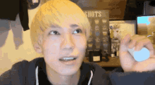 a young man with blonde hair is looking up at a sign that says shots