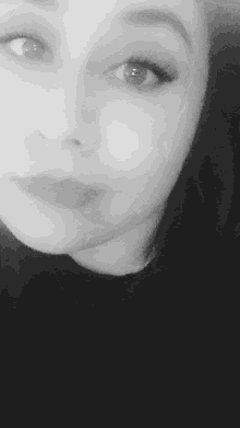 a woman is smiling in a black and white photo with her hand on her chin .
