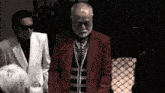a man in a red jacket is standing next to a man in a white suit