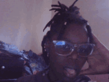 a man with dreadlocks is wearing sunglasses and his tongue is sticking out