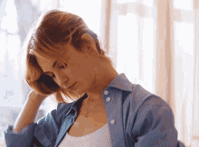 a woman wearing a white tank top and a blue shirt is looking down