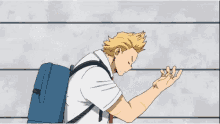 a man with a backpack is standing next to a wall with his arm outstretched .