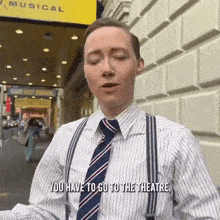 a man in a striped shirt and tie is standing in front of a building and talking .
