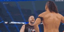 a man without a shirt is standing next to another man in a wrestling ring .