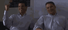 two men in white shirts are sitting next to each other in front of a whiteboard .