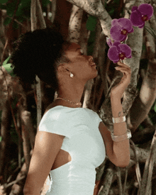 a woman in a white dress holds a purple flower in her hand