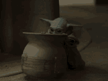 a figurine of a baby yoda is standing next to a vase