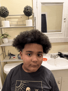 a young boy in a black shirt with a skull on it stands in front of a sink