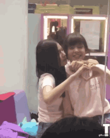 two girls are making a heart shape with their hands in front of a mirror with the letter t on it