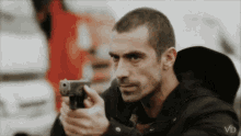 a man in a black jacket is pointing a gun at the camera
