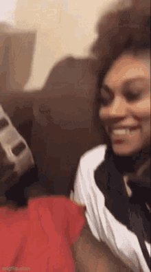 a woman is smiling while sitting on a couch next to a man in a red shirt .