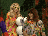 a man in a hawaiian shirt stands next to a woman holding a stack of eyeballs