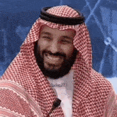 a man with a beard is wearing a keffiyeh and smiling while sitting in front of a microphone .