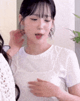 a woman in a white t-shirt holds her hand to her chest