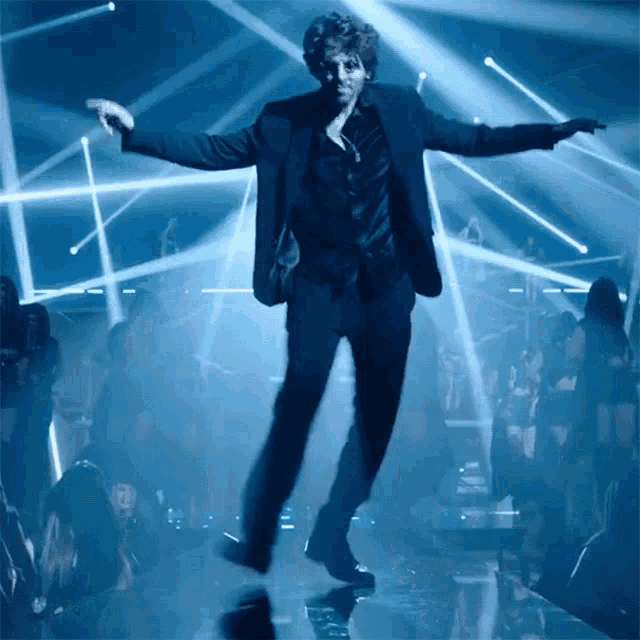 a man in a black suit is dancing in front of a crowd