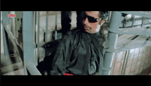 a man wearing sunglasses and a black jacket is standing next to a metal railing .
