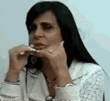 a woman with long black hair and a ring on her finger is sitting at a table with a glass of water .