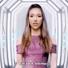 a woman in a purple dress is standing in front of a tunnel and saying i 'm back , bitches .
