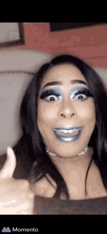 a woman with blue makeup is giving a thumbs up sign