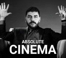 a man in a suit sits in a chair with his hands in the air and the words absolute cinema above him