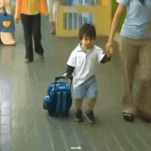 a little boy is pulling a blue suitcase while holding someone 's hand