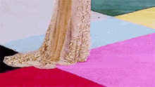 a woman in a long gold dress is standing on a red carpet .
